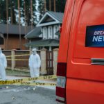 Forensic investigators in protective suits work at a marked-off crime scene near concrete houses. — Methmeth Casino: Mobile S