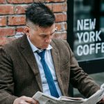 Man in formal attire reading a newspaper outside New York coffee shop. — test123123