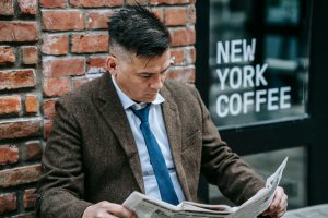 Man in formal attire reading a newspaper outside New York coffee shop. — test123123
