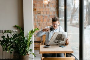 Man sitting indoors with coffee and newspaper, surrounded by plants by the window. — Transparente Zahlungsabwicklungen im Hig