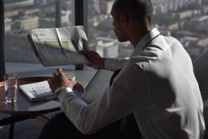 Businessman in office reading sports section, enjoying coffee with city view. — Was erwartet neue Spieler im Wheelz Casino?